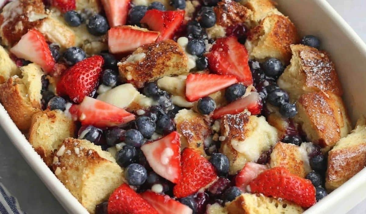 erry French Toast Casserole in a white ceramic dish topped with baked berries and powdered sugar