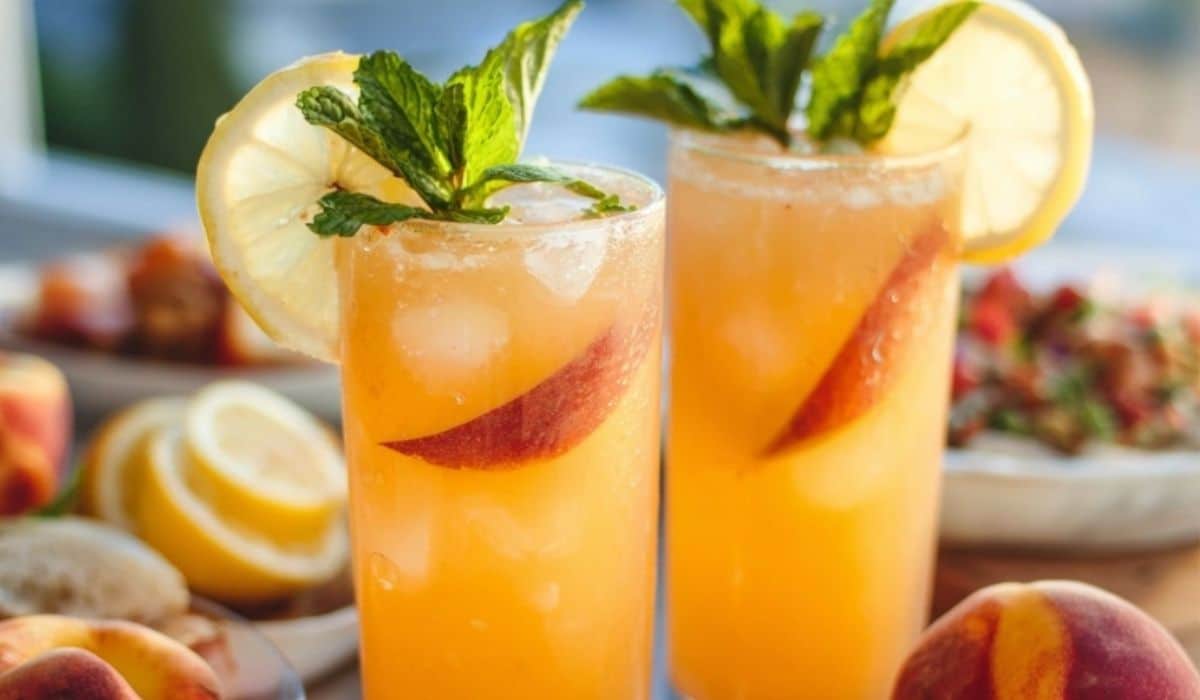 Peach lemonade in a glass pitcher with ice, peaches, and lemon slices